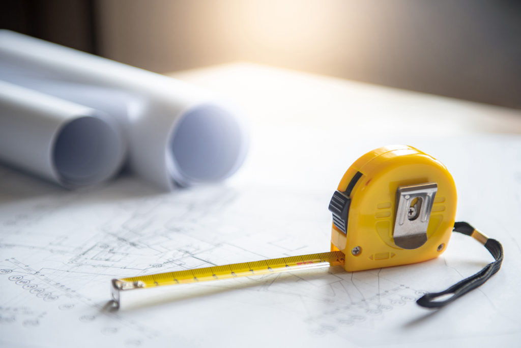 Architectural drawing plan of house project, blueprint rolls and yellow tape measure (measuring tape) on working table, Architecture and building construction industry concepts